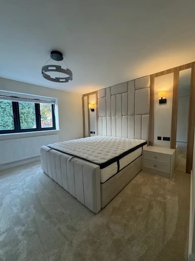 Upholstered panelled bed wall with timber framing, fitted bedsides and wall lights